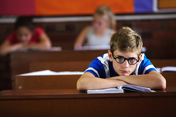 Image showing Education, classroom and bored with a boy student or nerd at desk, listening to lesson for growth or development. School, book and learning with young adhd child in class to study for an exam or test