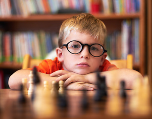 Image showing Chess, thinking or bored with a boy student learning how to play a boardgame at school for education. Face, strategy and glasses with a young student child in a classroom for intelligence development