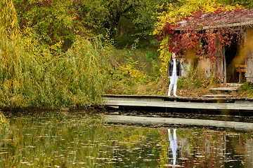 Image showing A young beautiful girl walks by the lake in an autumn park