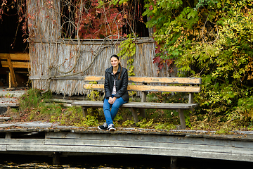 Image showing A young beautiful girl in casual clothes sits on a bench in an autumn park