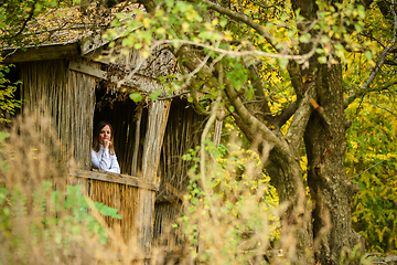 Image showing A young beautiful girl looks out of the window of an old abandoned house in the forest