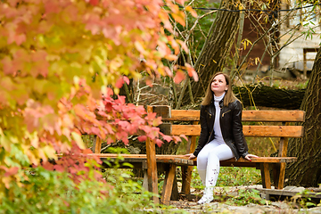 Image showing A young beautiful girl sits on a bench and enjoys the autumn landscape