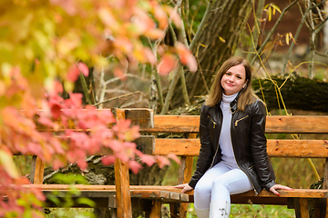 Image showing A young beautiful girl sits on a bench in an autumn park