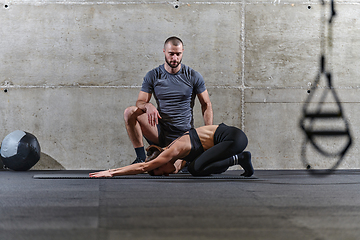 Image showing A muscular man assisting a fit woman in a modern gym as they engage in various body exercises and muscle stretches, showcasing their dedication to fitness and benefiting from teamwork and support