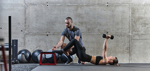 Image showing A muscular man assisting a fit woman in a modern gym as they engage in various body exercises and muscle stretches, showcasing their dedication to fitness and benefiting from teamwork and support