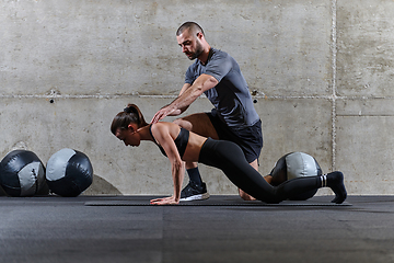 Image showing A muscular man assisting a fit woman in a modern gym as they engage in various body exercises and muscle stretches, showcasing their dedication to fitness and benefiting from teamwork and support