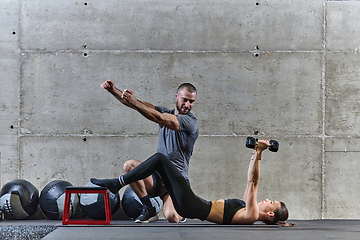 Image showing A muscular man assisting a fit woman in a modern gym as they engage in various body exercises and muscle stretches, showcasing their dedication to fitness and benefiting from teamwork and support