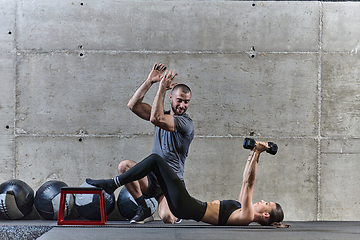 Image showing A muscular man assisting a fit woman in a modern gym as they engage in various body exercises and muscle stretches, showcasing their dedication to fitness and benefiting from teamwork and support