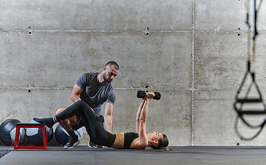 Image showing A muscular man assisting a fit woman in a modern gym as they engage in various body exercises and muscle stretches, showcasing their dedication to fitness and benefiting from teamwork and support