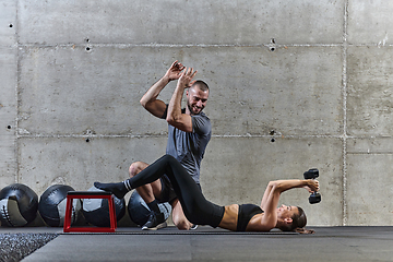 Image showing A muscular man assisting a fit woman in a modern gym as they engage in various body exercises and muscle stretches, showcasing their dedication to fitness and benefiting from teamwork and support