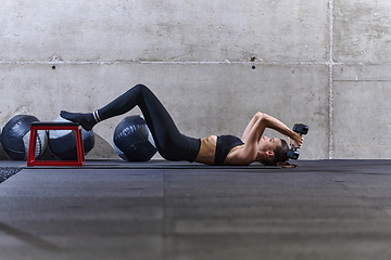 Image showing A fit woman is lying on the gym floor, performing arm exercises with dumbbells and showcasing her dedication and strength.