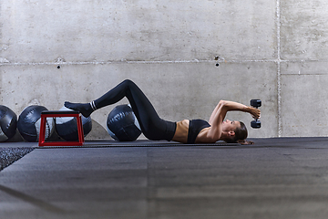 Image showing A fit woman is lying on the gym floor, performing arm exercises with dumbbells and showcasing her dedication and strength.