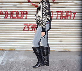 Image showing Boots, fashion and body of young woman by garage door for stylish, cool and edgy outfit with jeans. Legs, feet and zoom of female person with cigarette and trendy grungy style by steel background.