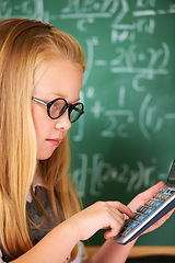 Image showing Child, learning math and board in classroom for problem solving, typing numbers and calculation with glasses. Smart student or girl with calculator for education, knowledge and solution on chalkboard