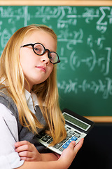 Image showing Child, portrait and calculator by chalkboard for education, learning and problem solving or solution with confidence. Smart kid, student or girl with glasses for school, numbers and math in classroom