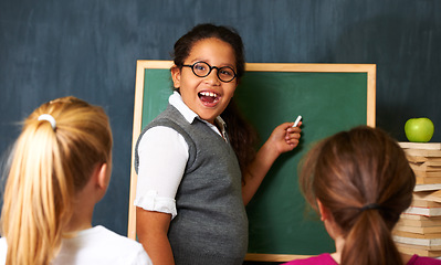 Image showing Excited, board and portrait of child student in a classroom teaching a lesson to friends. Happy, smile and girl kid writing with chalk for education studying, learn or knowledge at school or academy.