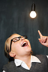 Image showing Student, child and lightbulb for solution, learning and wow, surprise or excited for future, ideas and knowledge in school. Girl kid thinking with light bulb, glow and black chalkboard for vision