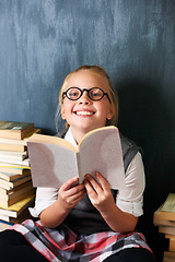Image showing Girl reading book, student and chalkboard for education, language learning and knowledge in classroom. Smart kid or child with glasses and happy for school library, fiction and literature in portrait