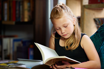 Image showing Girl, child and library for reading book, education and learning of language, literature and fiction story on sofa. Kid relax in bookstore with novel for creative development, knowledge and school