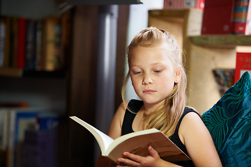 Image showing Girl, kid and library for reading book, education and learning of language, literature and fiction story on sofa. Child relax in bookstore with novel for creative development, knowledge and school