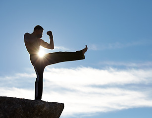 Image showing Karate, fitness man kick on mountain top for body, power or defense training on blue sky background. Martial arts, MMA and male taekwondo master in nature for exercise, sports or morning cardio