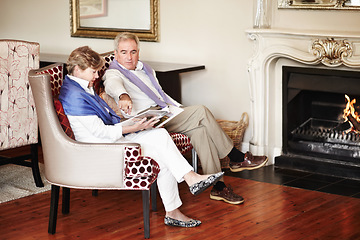 Image showing Senior couple, relax and reading by fire place on holiday, retirement or vacation together at hotel or resort. Man and woman sitting with magazine or paper for news, deals or activities at house