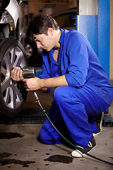 Image showing Mechanic, man and change wheel in shop, electric drill and car service or auto repairs for maintenance. Technician, male person and tire safety for automobile, rim and vehicle inspection in workshop