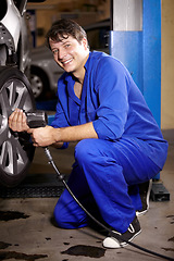 Image showing Mechanic, man and smile by wheel in shop, electric drill and car service or repairs for maintenance. Technician, male person and tire change for automobile, rim and vehicle inspection in portrait