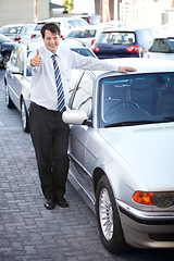 Image showing Portrait, thumbs up and a man at the dealership for a car sale, lease or rental in a commercial parking lot. Smile, retail or agreement with a happy young salesman working in the vehicle trade