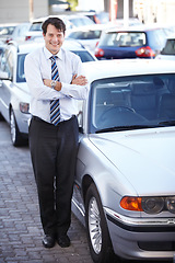 Image showing Portrait, lease and a man arms crossed at a dealership for car sale in a commercial parking lot. Business, rental and automobile trade with a happy young salesman outdoor for transport service