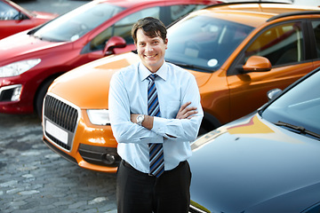 Image showing Portrait, smile and a man arms crossed at a dealership for car sale in a commercial parking lot. Business, luxury and automobile trade with a happy young salesman outdoor for transport service