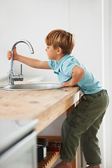 Image showing Kids, fantasy and a boy in the kitchen sink, playing a game in his home as a plumber character. Children, basin and counter with a young male kid in a modern apartment for imaginary plumbing