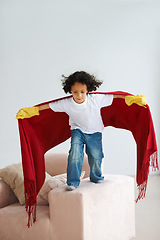 Image showing Jump, children and a boy superhero in a costume on a sofa in the living room of his home for playing a game. Flying, growth and fantasy with a young kid in a cape for justice or safety cosplay