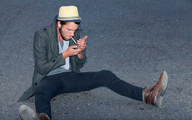 Image showing Hipster, man and sitting in road with cigarette for smoking, fashion or experience outdoor on ground. Person, smoke and street for adventure, travel or downtown with tobacco, light and confidence