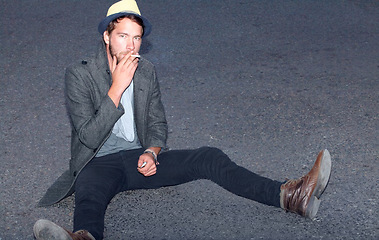 Image showing Portrait, outdoor and man smoking, hipster on the ground and relax with fashion, casual and stylish. Person, outdoor and guy with cigarette, tobacco and smoke with casual, trendy and outfit clothes