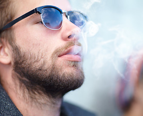 Image showing Face, man and smoking with sunglasses for experience, fun and cigarette enjoyment outdoor. Person, hipster and guy with smoke for exhale, serious and smoker with tobacco satisfaction and shades