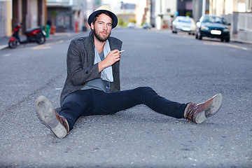 Image showing Portrait, outdoor and man smoking, fashion on the ground and relax with trendy clothes, New York and stylish. Person, outdoor and guy with cigarette, tobacco and smoke with casual, outfit and city