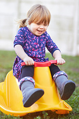 Image showing Baby, girl and outdoor on rocker with smile on grass for learning, game and development in family garden. Youth child, toddler and plastic toys for playing, happy or backyard lawn in summer sunshine