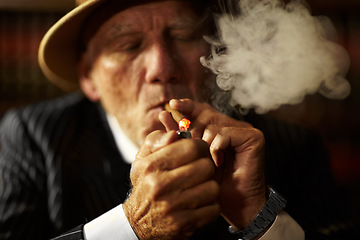 Image showing Mature, man and cigarette with lighter for smoking to relax in space. Elderly person, mob boss or gangster with suit, hat and serious face for habit, hand and puff for meeting in criminal activity
