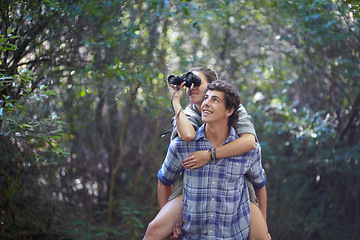 Image showing Man, woman and piggyback outdoor with binocular for travel, adventure or sightseeing in nature with happiness. Couple, people and tourist hiking in woods or forest for experience, holiday or vacation