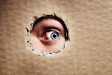 Image showing Closeup, cardboard and eye spy on hole, peek and search on mockup space. Face, macro and man peeping through paper board for secret, security and watch for surveillance, discover mystery and privacy