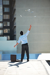 Image showing Back, financial freedom and money rain with a businessman in the city, throwing cash during a summer day. Finance, success or raining dollars with a person on the roof of a building in an urban town