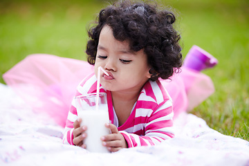 Image showing Kid, girl and lying on grass with milk for drinking by straw in pink tutu, princess or dress up. Child, youth and curly hair with calcium for development, growth and strong bones with healthy diet