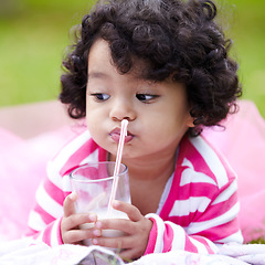 Image showing Child, milk and glass with straw on grass for drink of dairy while lying for picnic in park. Girl, pink tutu and thinking of delicious beverage for growth, development and nutrition high in calcium