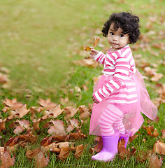 Image showing Portrait, child and playing in tutu on grass with brown leaves in autumn. Face, adorable kid and curly hair with rain boots outside for development, education and learning of seasons in environment