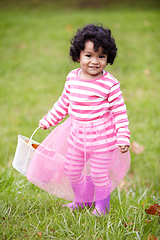 Image showing Portrait, happy child and tutu on grass in park with basket for leaves for autumn. Little girl, pink clothes and curly hair with rain boots for growth, development and changing of season for Easter