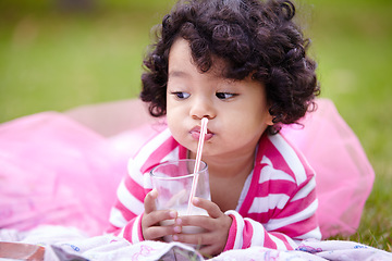 Image showing Girl, child and drinking of milk on grass with straw in pink tutu while lying for picnic. Youth, curly hair and kid with dairy for balanced diet, nutrition and calcium for development of strong bones