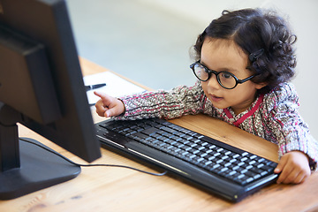 Image showing Playing, learning and a child reading from a computer for communication, education or the web. House, pretend work and a girl, kid or baby with a pc at a home table for play, smile and the internet