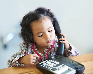 Image showing Playing, serious and a child on a telephone phone call for communication in a house. Home, contact and a girl, kid or baby listening on a landline for conversation, play or a discussion at a desk
