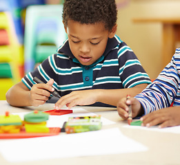 Image showing African boy, learning and writing at kindergarten with paper, crayon and thinking of sketch for art in classroom. Preschool kids, drawing and color at desk for development, scholarship and education